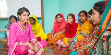 A group of women seated on the floor sit cross-legged and listen intently to one another during a discussion of vocational training of working teenagers in Bangladesh. Save the Children supports programs around the world aimed at changing dangerous working conditions for children. Photo credit: Save the Children, March 2017. A group of women seated on the floor sit cross-legged and listen intently to one another during a discussion of vocational training of working teenagers in Bangladesh. Save the Children supports programs around the world aimed at changing dangerous working conditions for children. Photo credit: Save the Children, March 2017.