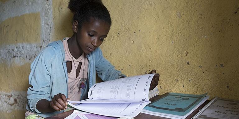 A teenage girl sits at a desk reading a book. A teenage girl sits at a desk reading a book.