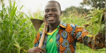 A Youth in Action program graduate student named Kassoum proudly stands in a field in Burkina Faso that is brimming with large, green crops. As the sun shines, Kassoum holds a large harvesting tool over his shoulder and smiles as he displays the freshly picked vegetables his year-round small farm produces. In partnership with Mastercard Foundation, Save the Children’s Youth in Action program works to improve the socio-economic status of over 40,000 out-of-school youth, girls and boys, aged 12-18 in rural Bu A Youth in Action program graduate student named Kassoum proudly stands in a field in Burkina Faso that is brimming with large, green crops. As the sun shines, Kassoum holds a large harvesting tool over his shoulder and smiles as he displays the freshly picked vegetables his year-round small farm produces. In partnership with Mastercard Foundation, Save the Children’s Youth in Action program works to improve the socio-economic status of over 40,000 out-of-school youth, girls and boys, aged 12-18 in rural Bu