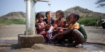 A group of children gather around a water spigot A group of children gather around a water spigot